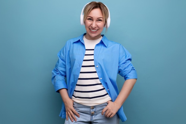 La ragazza bionda sorridente caucasica vestita con un maglione a righe e una camicia casual ascolta musica in