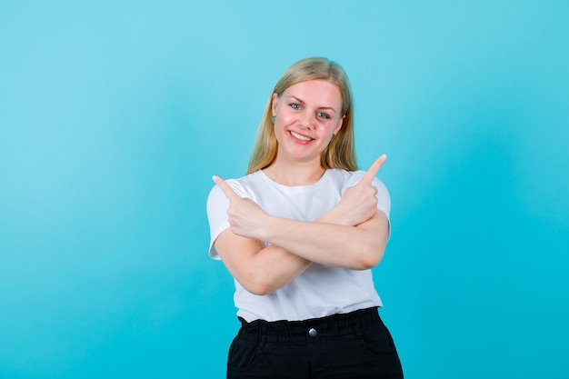 La ragazza bionda sorridente sta puntando a destra ea sinistra con gli indici su sfondo blu