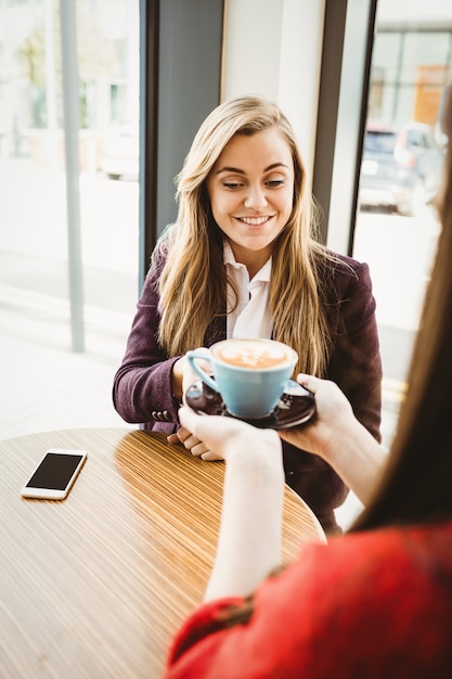 La ragazza bionda sveglia che mangia un caffè è servito dalla sua amica in una caffetteria