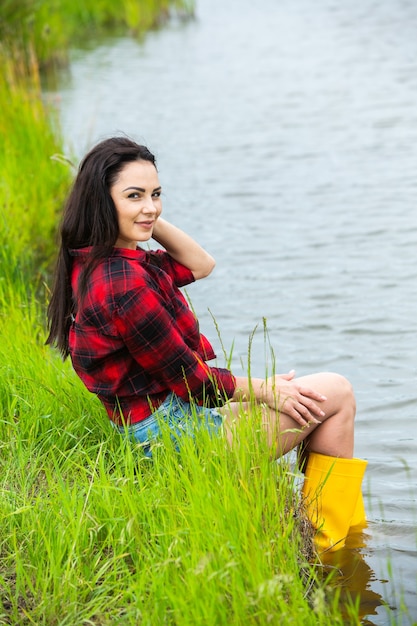 La ragazza bruna si diverte nel fiume con gli stivali di gomma in campagna La giovane donna su un lago si gode la vita