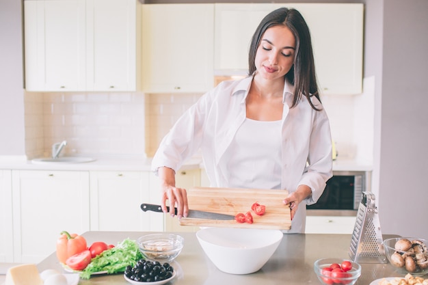 La ragazza calma e professionale sta mettendo la parte tagliata del pomodoro in ciotola.