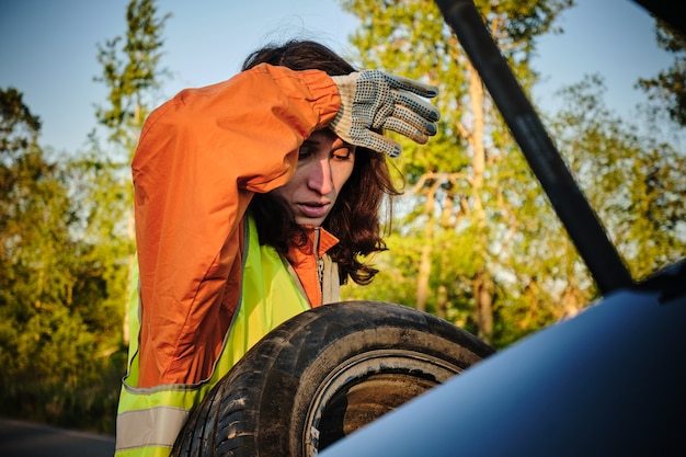 La ragazza cambia la ruota danneggiata dell'auto Gilet verde Ruota di scorta Incidente stradale