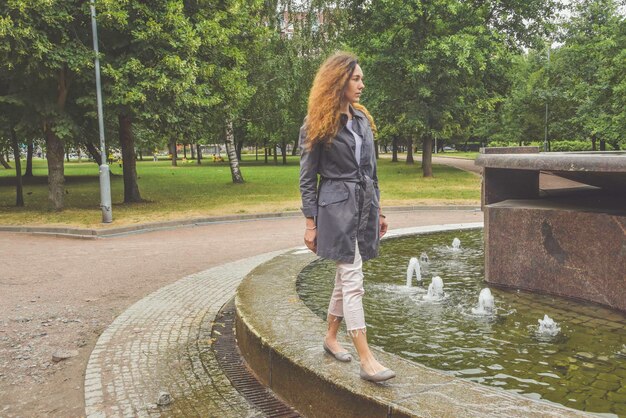 La ragazza cammina lungo il bordo di una fontana in un parco in una giornata di sole