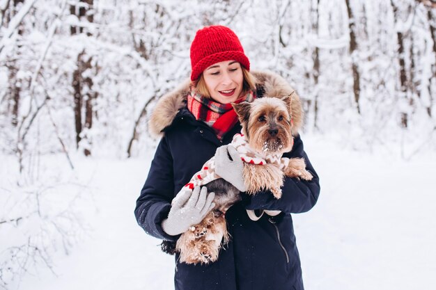 La ragazza cammina nei boschi inferiori in inverno con il cane che indossa un maglione di Natale