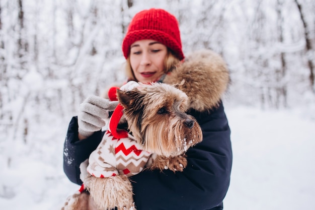 La ragazza cammina nei boschi inferiori in inverno con il cane che indossa un maglione di Natale