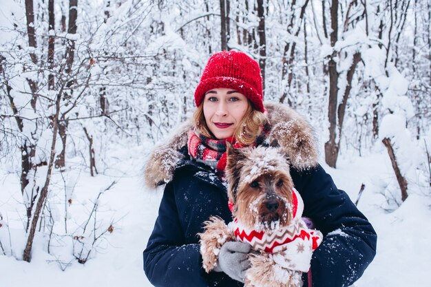 La ragazza cammina nei boschi inferiori in inverno con il cane che indossa un maglione di Natale