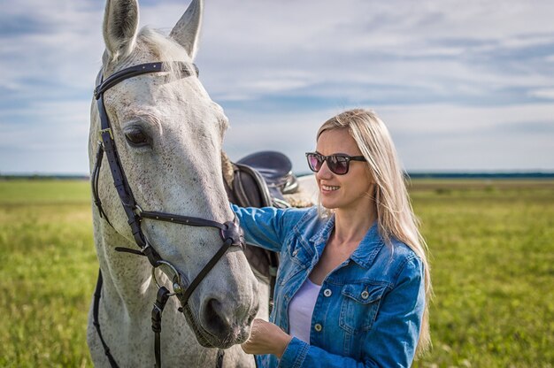 La ragazza cammina nel campo con un cavallo bianco