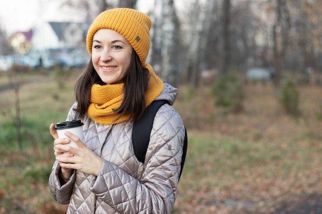 La ragazza cammina nel parco autunnale con una tazza di caffè