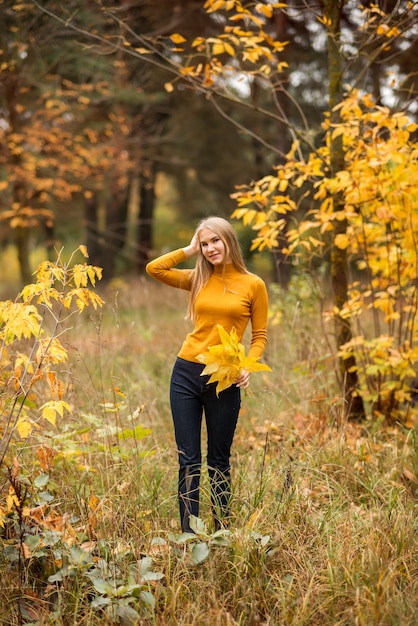 La ragazza cammina nella foresta autunnale. Una giovane donna su uno sfondo di foglie gialle e arancioni