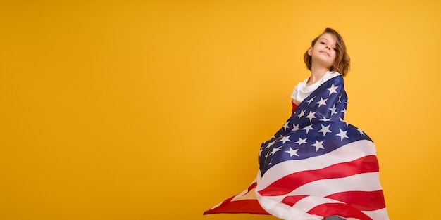 La ragazza carina del bambino felice con la bandiera americana sugli stati uniti gialli celebra il giorno dell'indipendenza