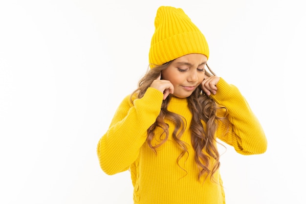 La ragazza caucasica felice in cappello e maglia con cappuccio gialli non vuole sentire isolata su bianco