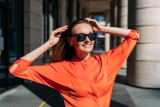 La ragazza caucasica in occhiali da sole e abbigliamento casual si rallegra del tempo soleggiato.