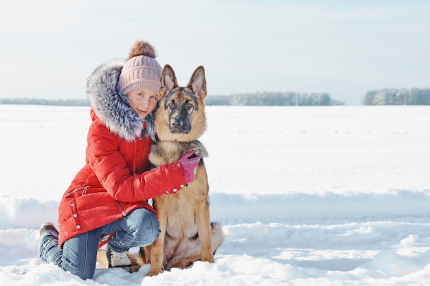 La ragazza che abbraccia il suo amato cucciolo nel parco innevato. Cane da pastore tedesco e bambino sul bianco della neve nella giornata invernale. Cura degli animali. Stile di vita.