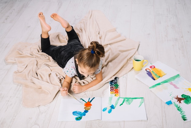 La ragazza che disegna dai colori di acqua su carta vicino disegna e trovandosi sul pavimento