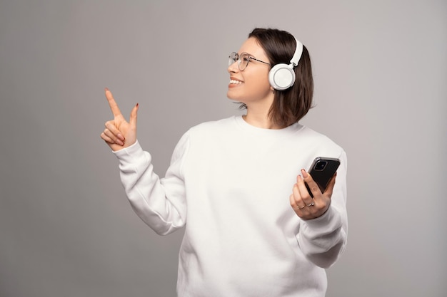 La ragazza che guarda in alto e indossa le cuffie punta da parte e tiene il telefono