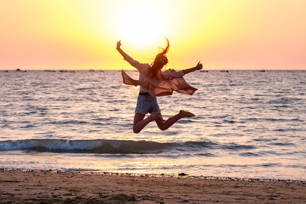 La ragazza che salta sulla spiaggia al tramonto dell'estate.