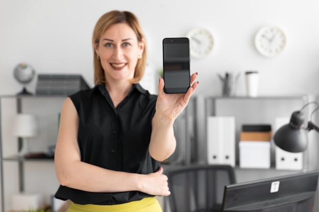 La ragazza che sta nell'ufficio e mostra lo schermo del telefono.