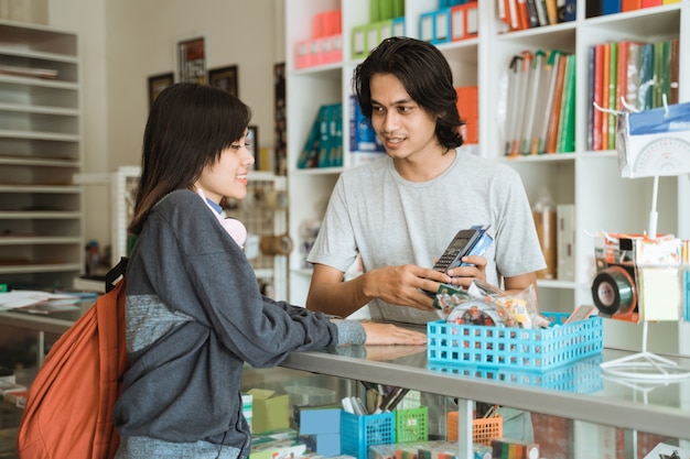 La ragazza che visita una cartoleria parla al cassiere maschio dei prezzi