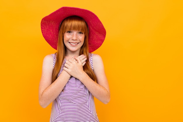 La ragazza con capelli rossi e cappello rosa sorride e spera per qualcosa di isolato su giallo