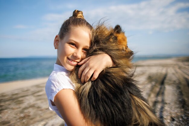 La ragazza con i capelli biondi con il sorriso abbraccia il cane pomeranian con i capelli dorati in riva al mare vicino al Mar Nero