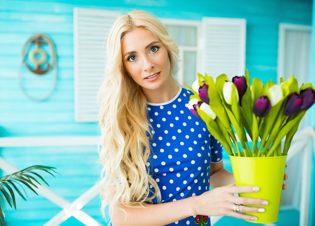 La ragazza con i capelli biondi e gli occhi chiusi tiene in mano un vaso con tulipani bianchi e viola