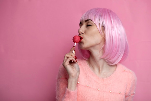 La ragazza con i capelli corti rosa lecca e succhia i chupachups con il concetto sexy di piacere