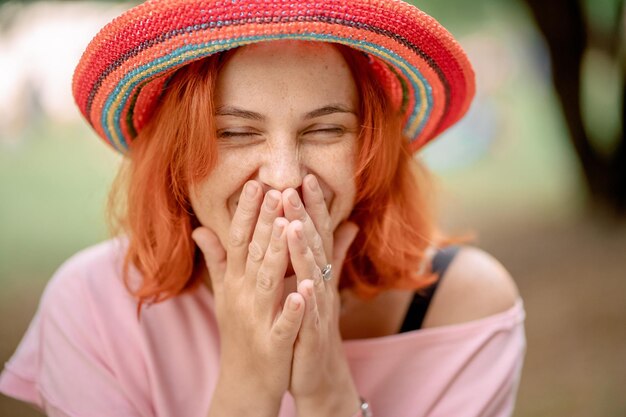 La ragazza con i capelli rossi in un cappello ride e si copre il viso con le mani