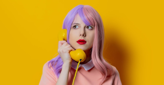 La ragazza con i capelli viola e il vestito rosa tiene il telefono su sfondo giallo