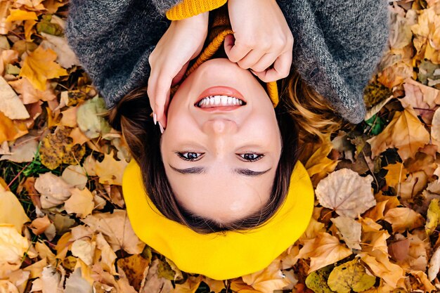 La ragazza con il berretto giallo sorride e si tocca il viso sulle foglie con la mano. Sconti