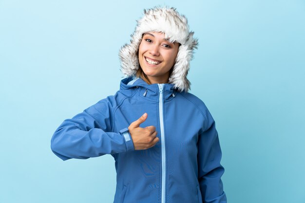 La ragazza con il cappello dell'inverno isolato sull'azzurro che dà pollici aumenta il gesto