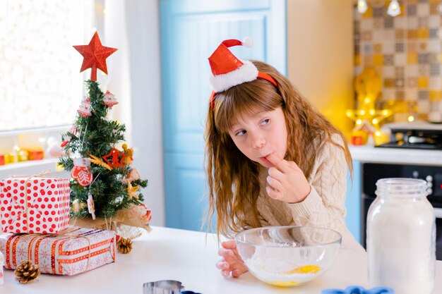 La ragazza con il cappello di natale lecca il dito con la farina