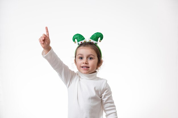 La ragazza con il cerchio a forma di cappello da elfo in testa mostra il dito verso l'alto.