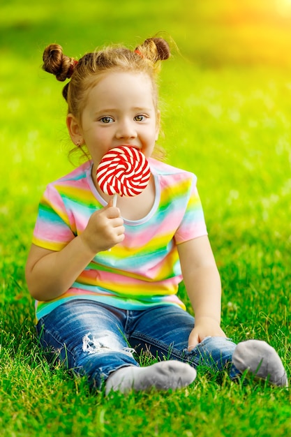 La ragazza con il lecca-lecca rosso si siede sull'erba estiva nel parco.