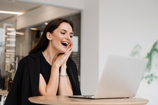 La ragazza con il sorriso sul laptop ride e discute di situazioni divertenti al lavoro con i colleghi Incontro video con amici e colleghi e divertiti online da remoto dopo il successo del progetto