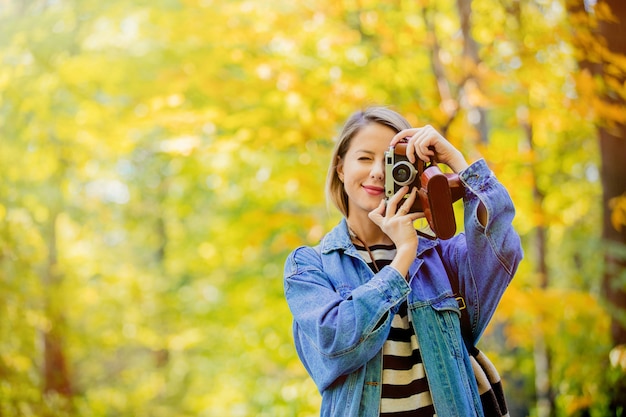 La ragazza con la macchina fotografica d'annata ha resto nel parco nel tempo di stagione di autunno