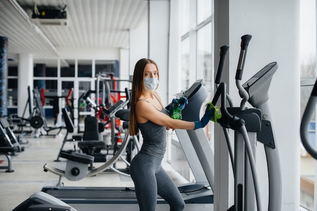 La ragazza con la maschera che disinfetta l'attrezzatura da palestra durante una pandemia