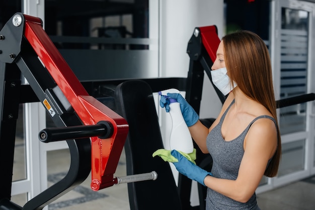 La ragazza con la maschera che disinfetta l'attrezzatura da palestra durante una pandemia.