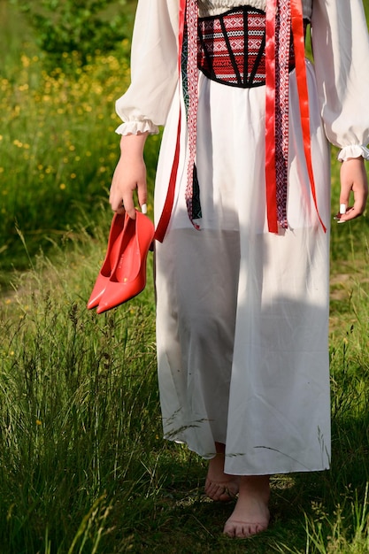 La ragazza con la schiena girata e vestita con abiti nazionali ucraini cammina a piedi nudi nel campo indossando una ghirlanda con nastri sulla testa