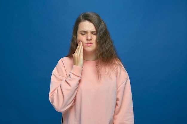 La ragazza con mal di denti tocca la guancia che soffre di improvviso dolore ai denti ha bisogno di aiuto dentale su blue studio