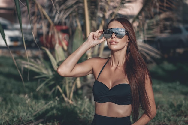 La ragazza con un corpo splendido sta riposando sulla spiaggia con sabbia bianca vicino all'oceano. Bello modello sexy in costume da bagno nero e occhiali da sole specchi per prendere il sole. Phuket. Tailandia. avvicinamento