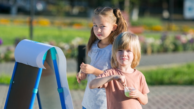 La ragazza con un fratello minore disegna le pitture sul parco di carta della città