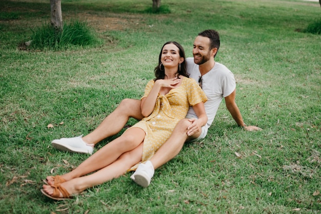 La ragazza con un vestito giallo è seduta tra le gambe del suo ragazzo sull'erba