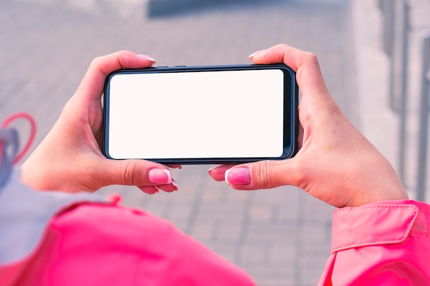 La ragazza con una giacca rosa tiene in mano un modello di smartphone con schermo bianco. Tecnologia di simulazione.