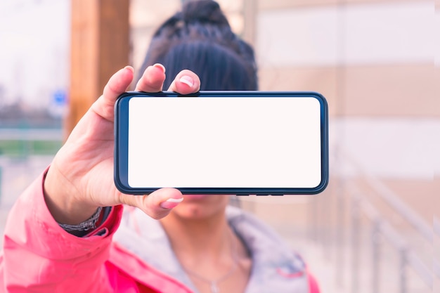 La ragazza con una giacca rosa tiene in mano un modello di smartphone con schermo bianco. Tecnologia di simulazione.