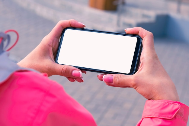 La ragazza con una giacca rosa tiene in mano un modello di smartphone con schermo bianco.