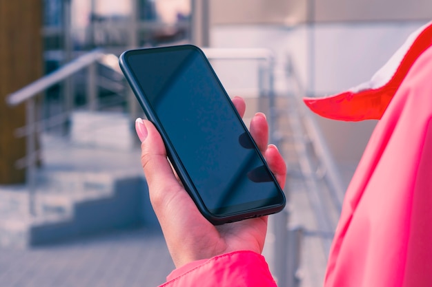 La ragazza con una giacca rosa tiene in mano un modello di smartphone. Tecnologia di simulazione.