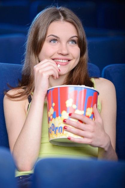 La ragazza con una grande scatola di popcorn mangia e guarda un film.