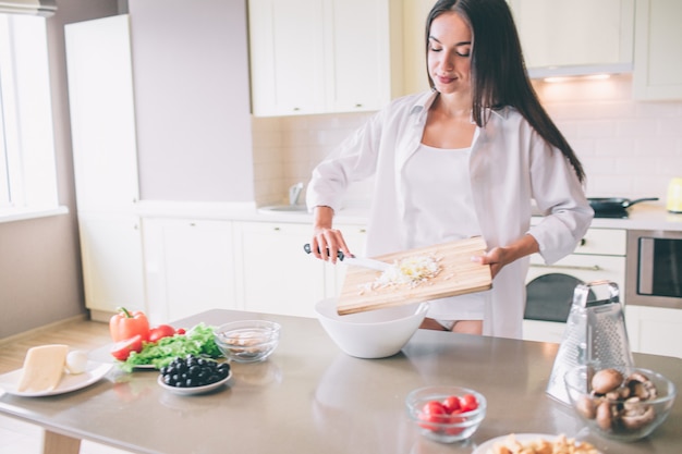 La ragazza concentrata sta cucinando la colazione. Sta mettendo il formaggio nella ciotola.