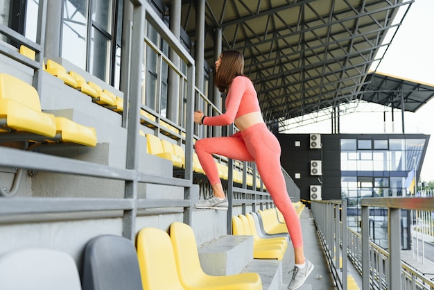 La ragazza corre di sopra verso un tramonto. Giovane donna in formazione di abbigliamento sportivo su uno stadio. Copia spazio. Stile di vita sano in un concetto di città