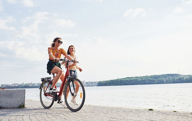 La ragazza corre vicino alla bicicletta. Due amiche in bici si divertono in spiaggia vicino al lago.